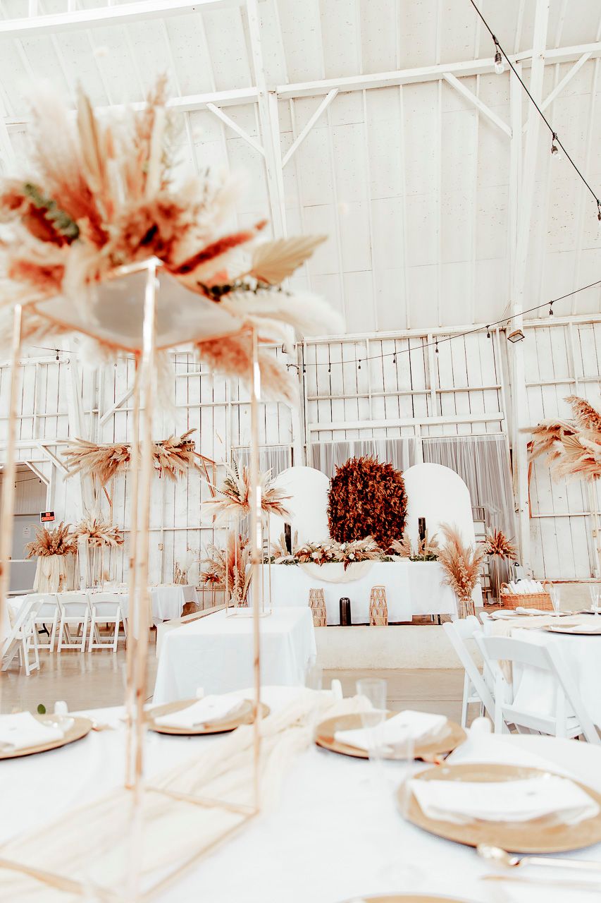 Elegant wedding reception venue with dried pampas grass centerpieces and white table settings in a bright, airy space.