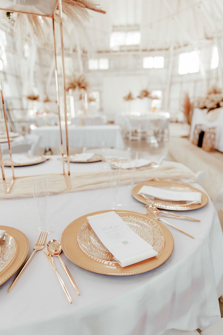 Close-up of a formal place setting with gold charger plates and white linens at an elegant event.