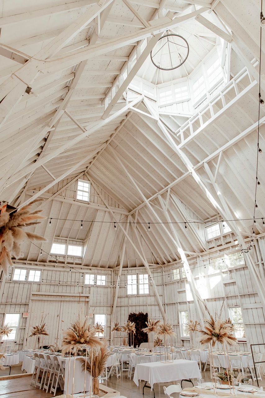 Interior of a white barn venue with vaulted ceiling, skylights and round tables set up for an elegant wedding reception.