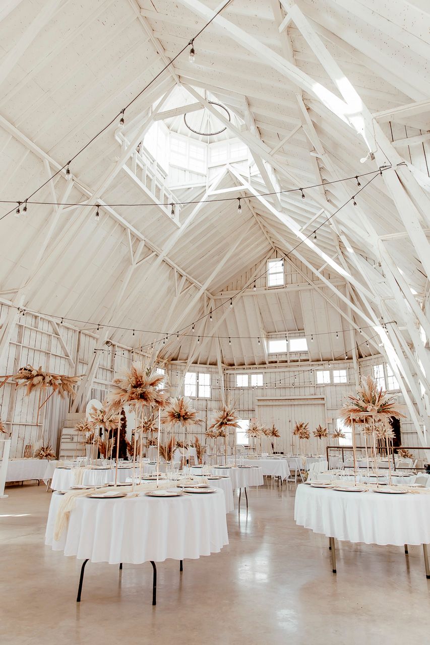 Elegant wedding reception venue with white cathedral ceilings, string lights, and dried floral centerpieces on round tables.