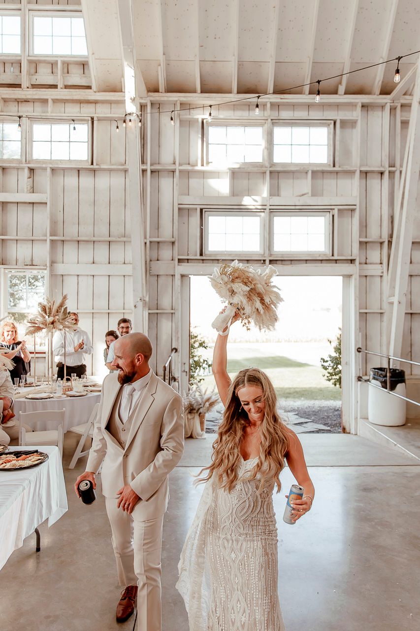 A modern white barn-style wedding venue interior with bright windows and couple celebrating on the dance floor.