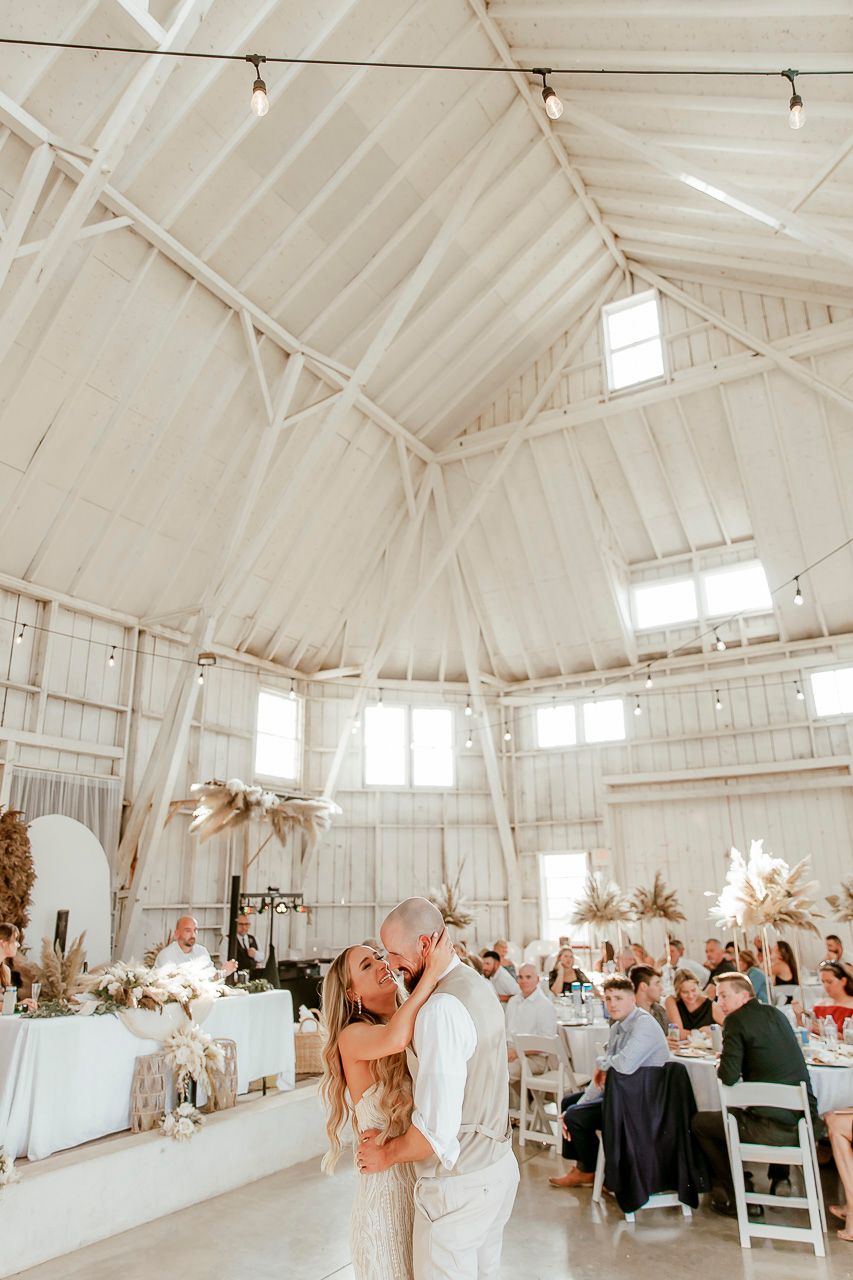 Elegant white barn wedding reception venue with vaulted ceilings, string lights and modern rustic decor.