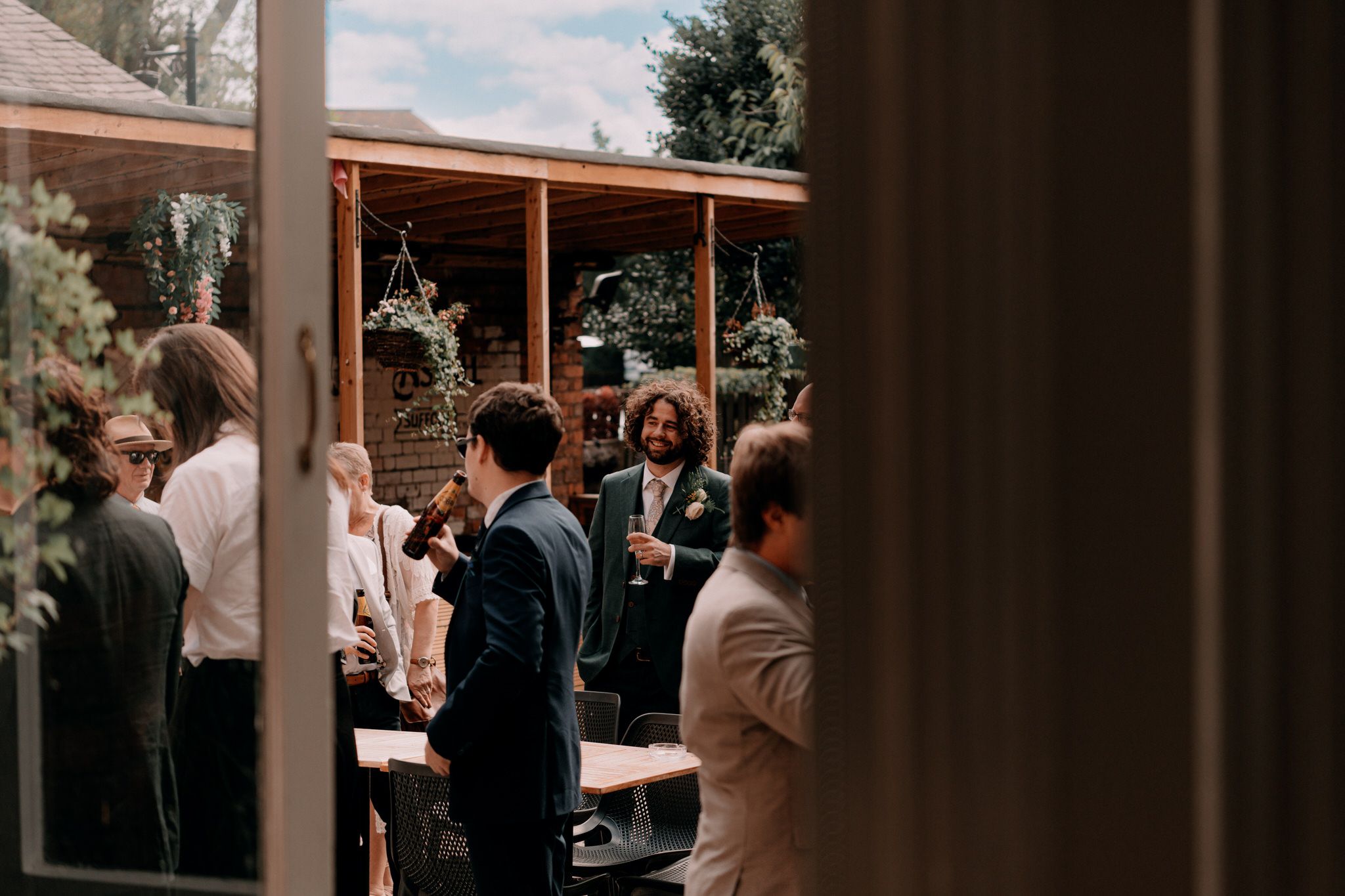 Guests mingle at an outdoor wedding reception under a covered patio area.