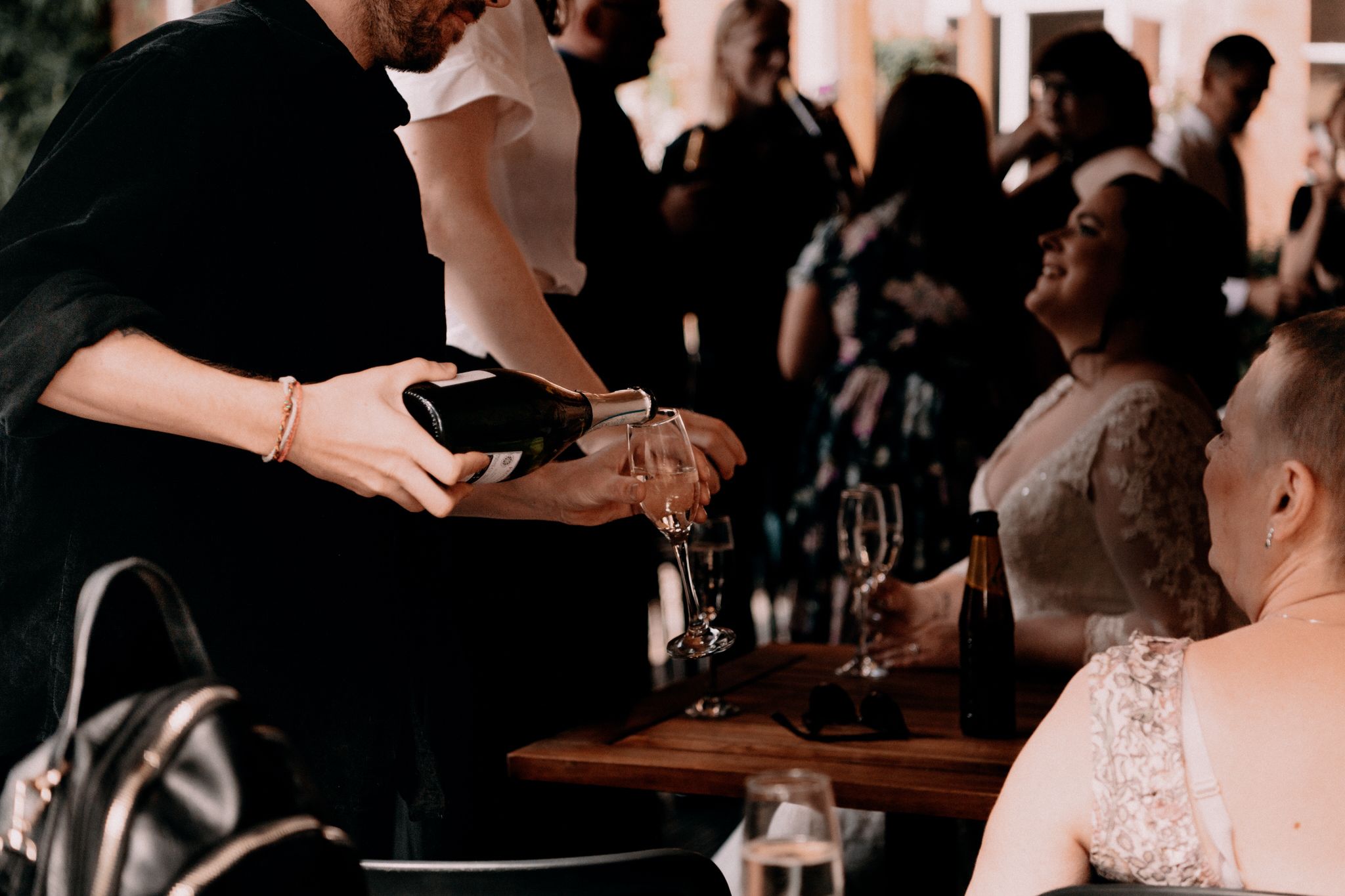 Server pours red wine into glass at busy restaurant bar during dinner service.