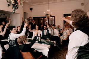 Wedding guests cheering and raising their hands during a celebratory moment at an indoor reception.