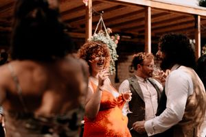 Party guests dancing and enjoying themselves at an outdoor wedding reception under wooden beams.