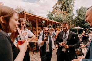 A group of guests socializing and laughing while enjoying drinks at an outdoor garden reception.