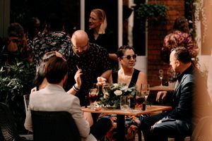 Wedding guests gathered around a table having animated conversations during an outdoor reception.