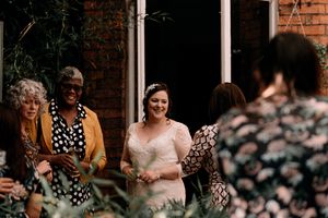 A group of wedding guests in colorful outfits gather on a porch near brick walls during a celebration.