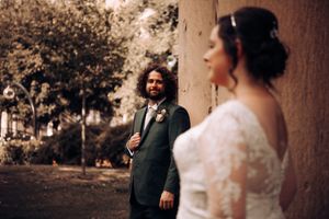 Two people in wedding attire stand outdoors against a stone wall in warm sepia tones on their special day.