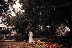 A figure in a white dress stands amid fallen autumn leaves in a backyard garden at sunset.