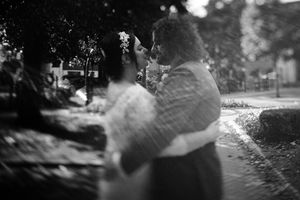 Black and white photograph showing someone holding a fluffy white cat outdoors on a sunlit path.
