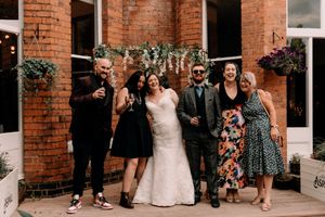 A small wedding party poses together in front of a rustic brick building with hanging plants.