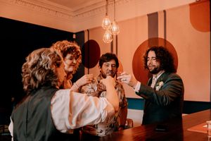 A group of friends raise their glasses together in a dimly lit bar with orange lighting and vintage decor.