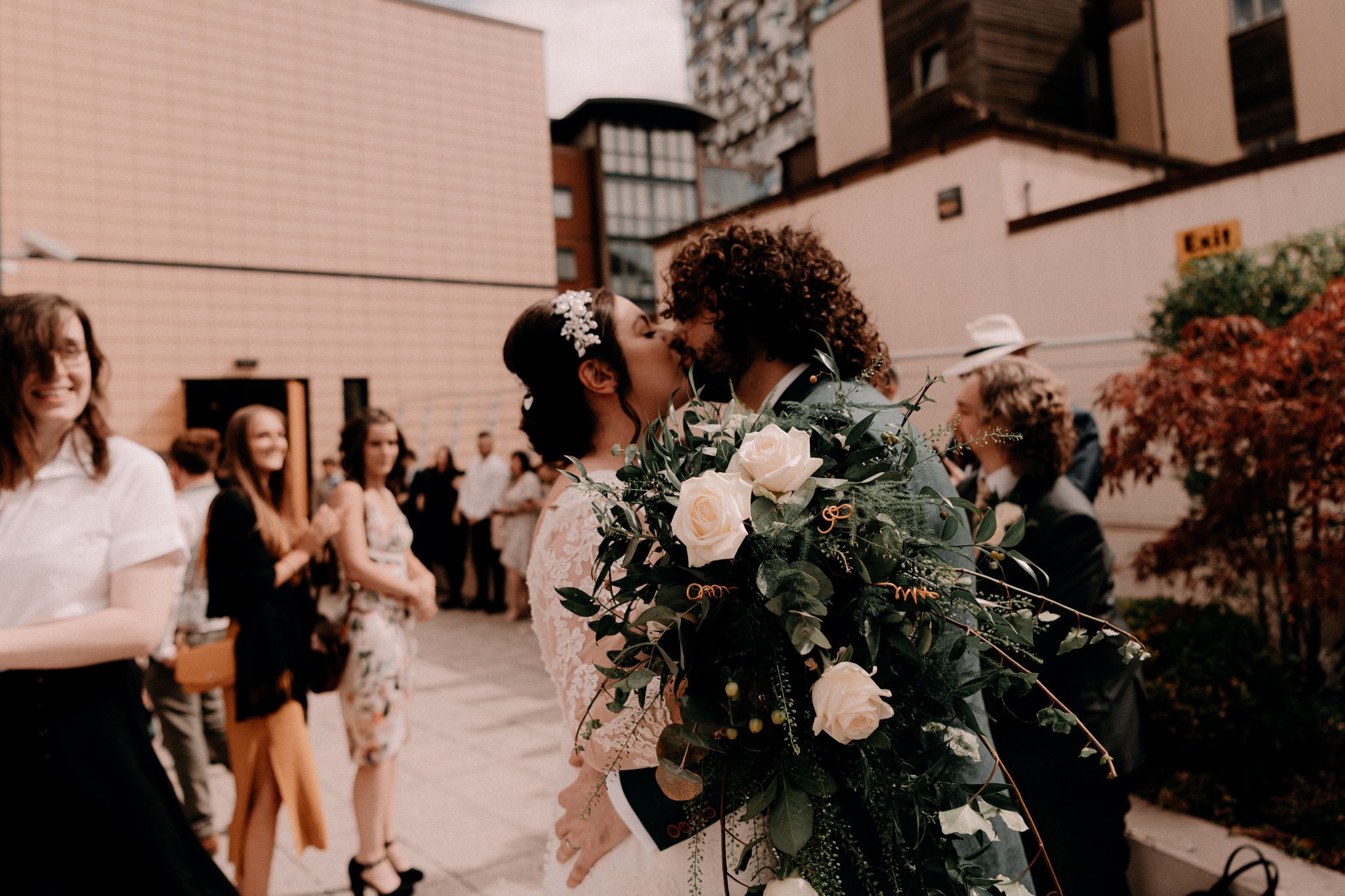 A group gathers outdoors at an urban wedding celebration with lush floral arrangements and decorative greenery.