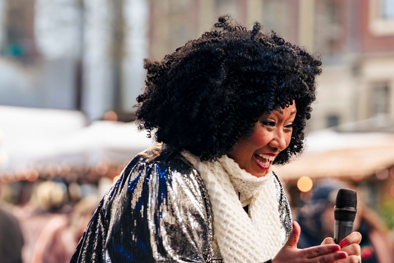 Portrait of a smiling person with natural curly hair holding a phone outdoors.