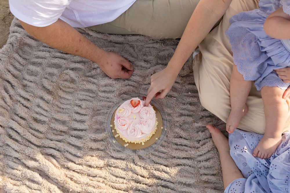 Aerial view of family sharing a strawberry birthday cake on a cozy blanket outdoors.