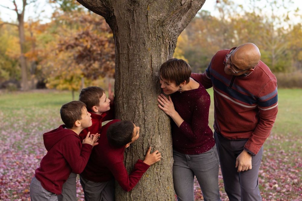 Playful family photo sequence near a large tree trunk in autumn.