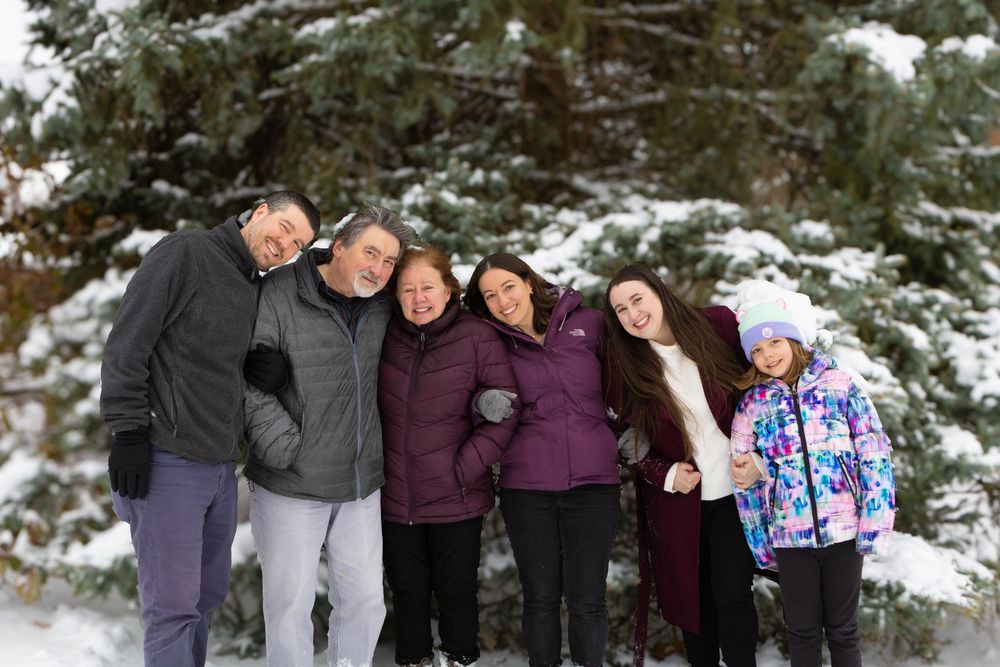 A group poses together in winter attire against a snowy evergreen forest backdrop.