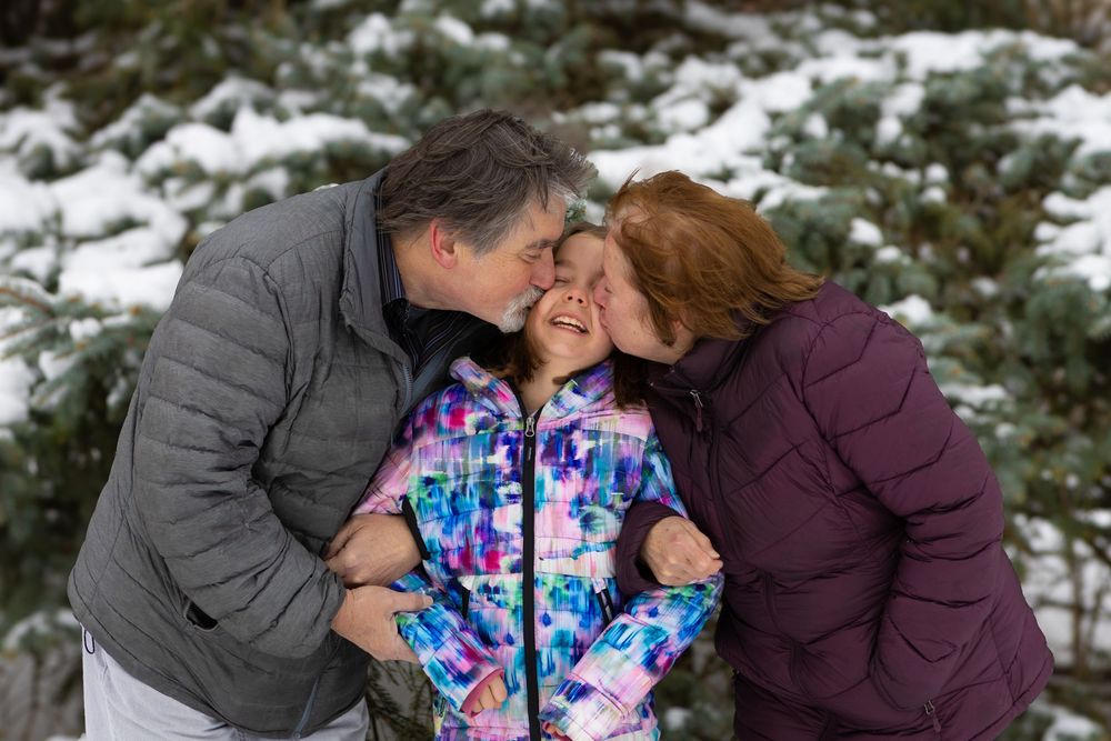 Family embracing in a snowy winter scene wearing colorful winter coats and jackets.