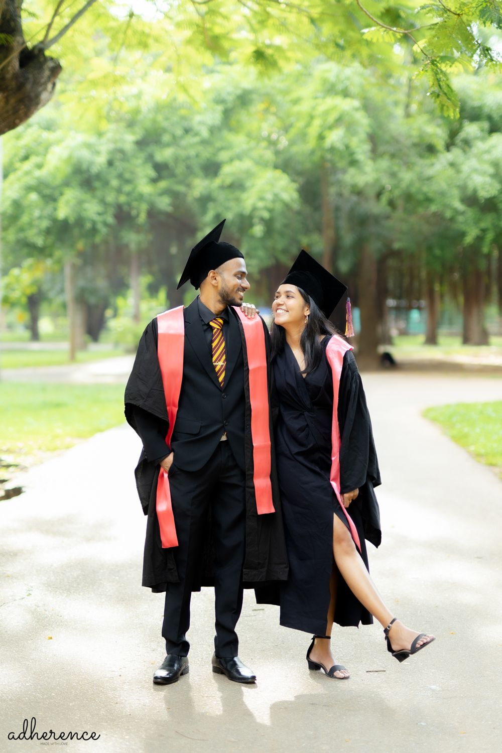 Two graduates in academic regalia share a joyful moment walking together outdoors.