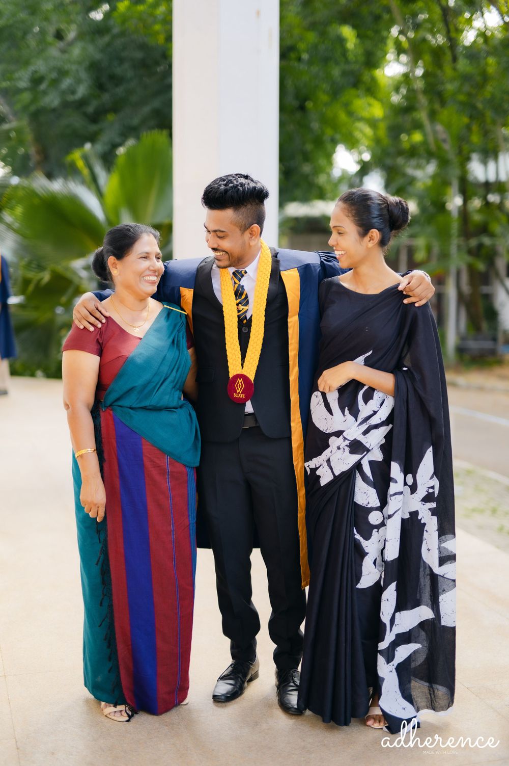 Graduation celebration with family members wearing traditional attire and academic regalia in an outdoor garden setting.