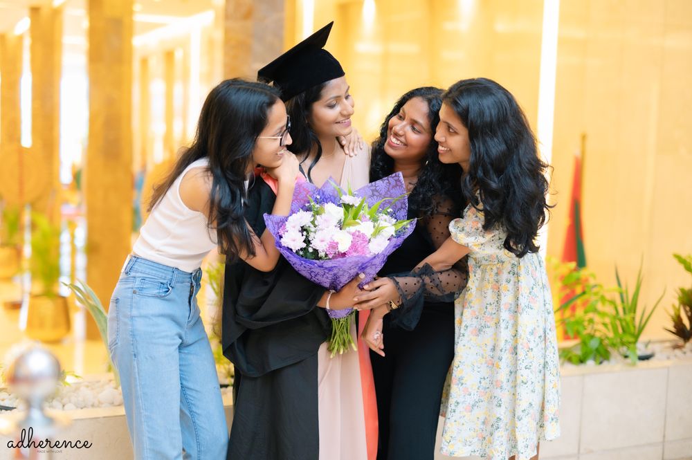 A graduation celebration with friends sharing joy and flowers in bright hallway.