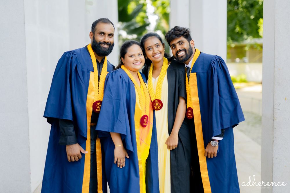 Group photo of graduates wearing blue and gold academic regalia standing together outdoors.