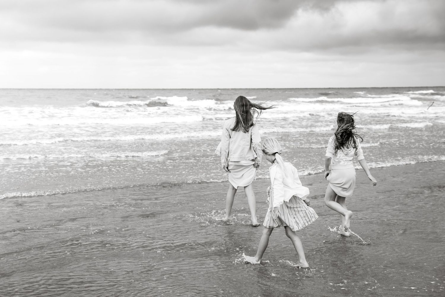 Family walks along beach shoreline in black and white as waves crash behind them.