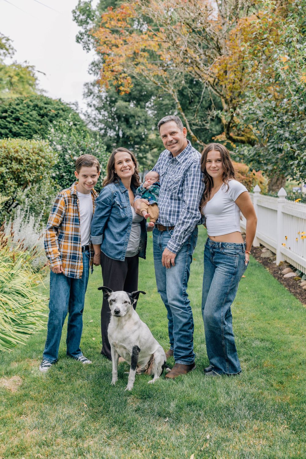 Family of five poses with a white dog in a lush green backyard on a fall afternoon.