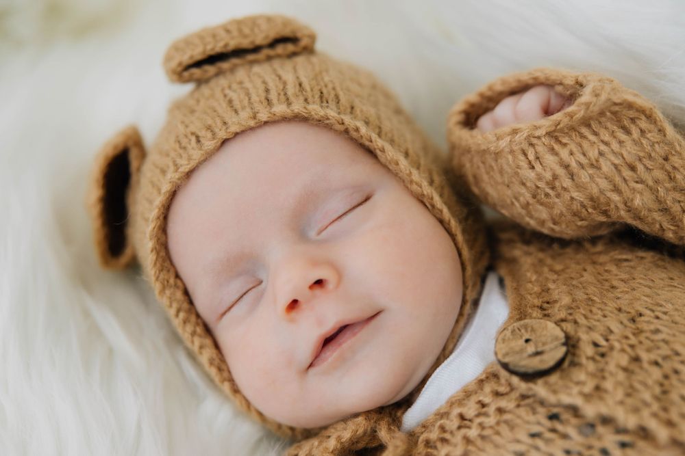 Sleeping newborn baby wearing a cozy brown knit bear outfit and hat.