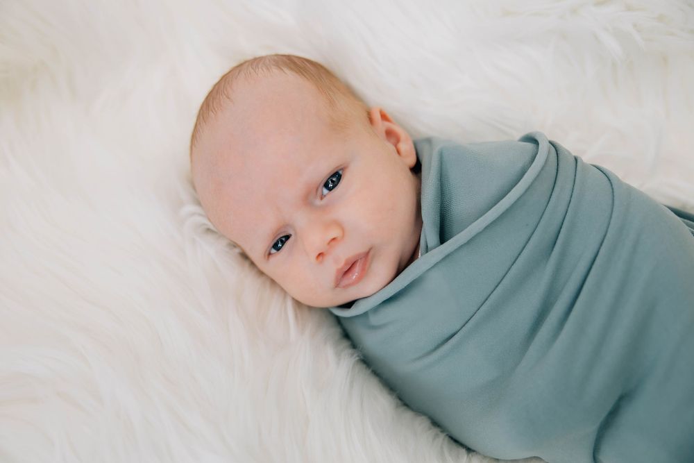 Newborn baby swaddled in a soft blue wrap lying on a white fluffy blanket.