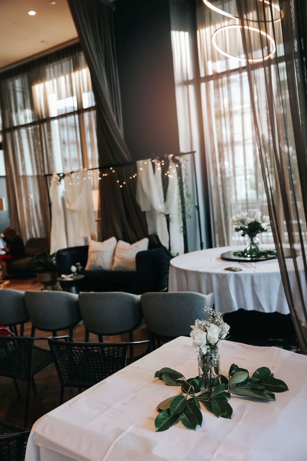Wedding reception venue with draped curtains, string lights, and elegant table settings with floral centerpieces.