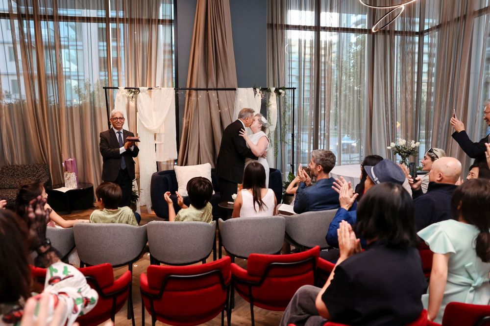 Candid moment during a wedding ceremony with guests seated in red chairs.