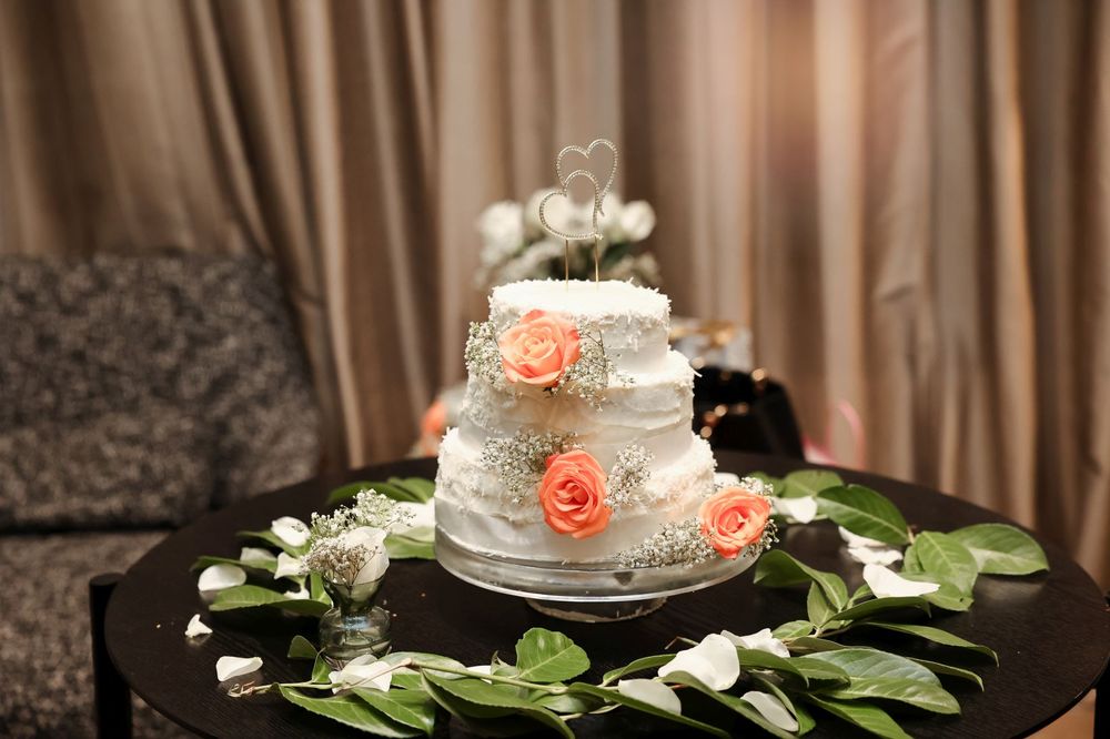Elegant three-tier wedding cake decorated with peach roses and greenery on a black table.