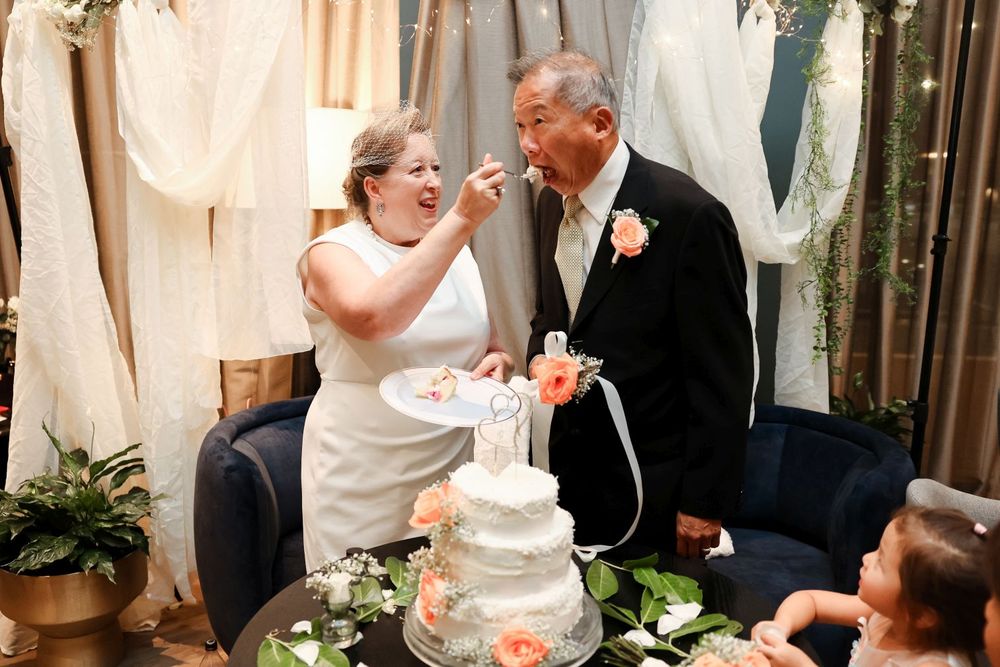 Couple shares a playful moment while feeding each other wedding cake at their reception.