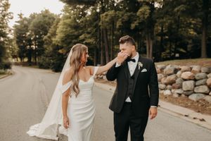 Emotional groom wiping tears as bride smiles during outdoor wedding photo session.