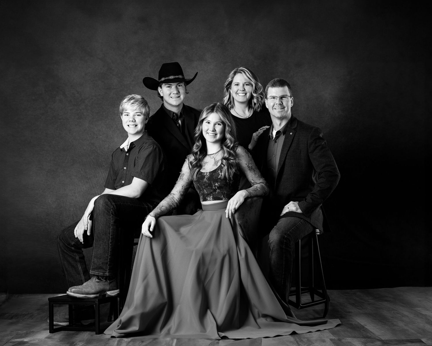 Elegant formal family portrait with four people in dark attire against black background. branding North Platte Nebraska Photographer