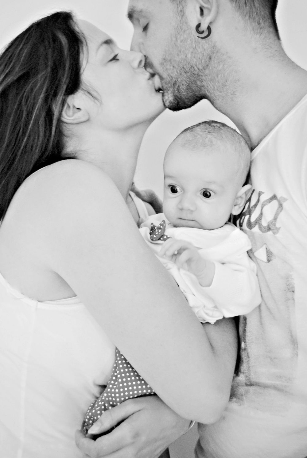An intimate black and white family portrait capturing a tender moment between parents and their baby.