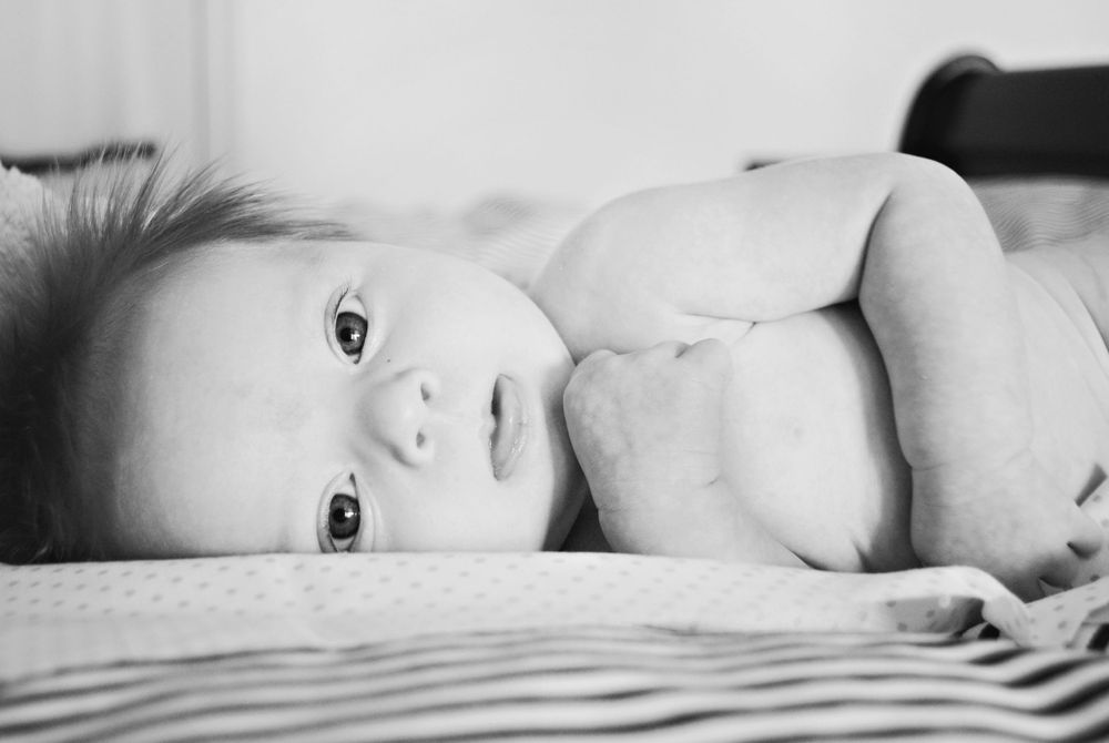 A close-up black and white portrait of a baby lying on their side with bright eyes.