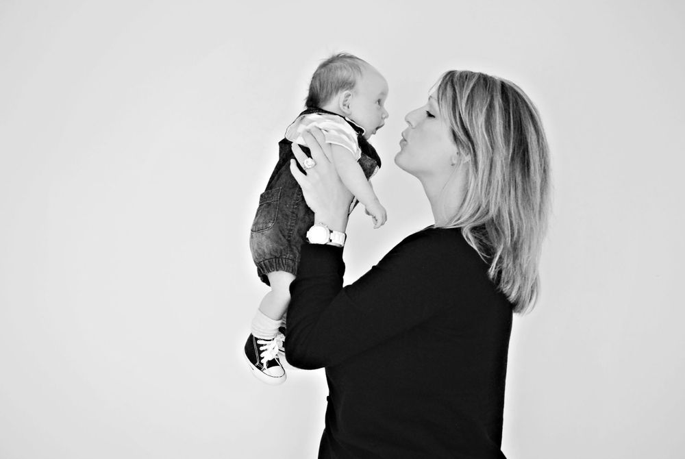 An intimate black and white photograph of a mother lifting her infant while sharing a joyful moment.