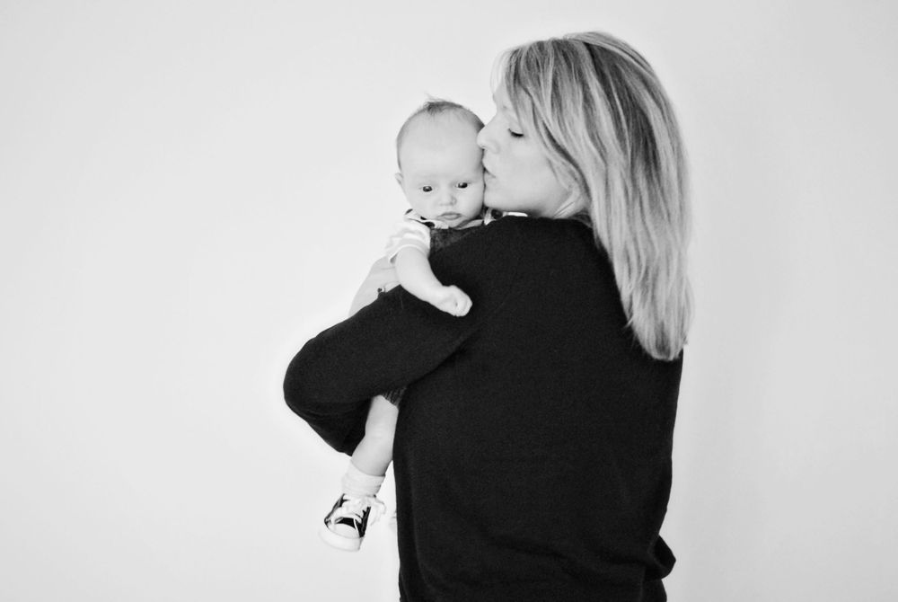 A monochrome side view of a mother in black sweater kissing her baby.