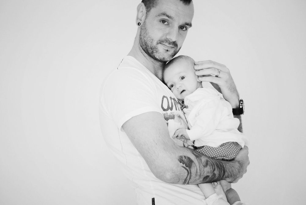 A black and white portrait showing a tender moment between a parent and small infant.