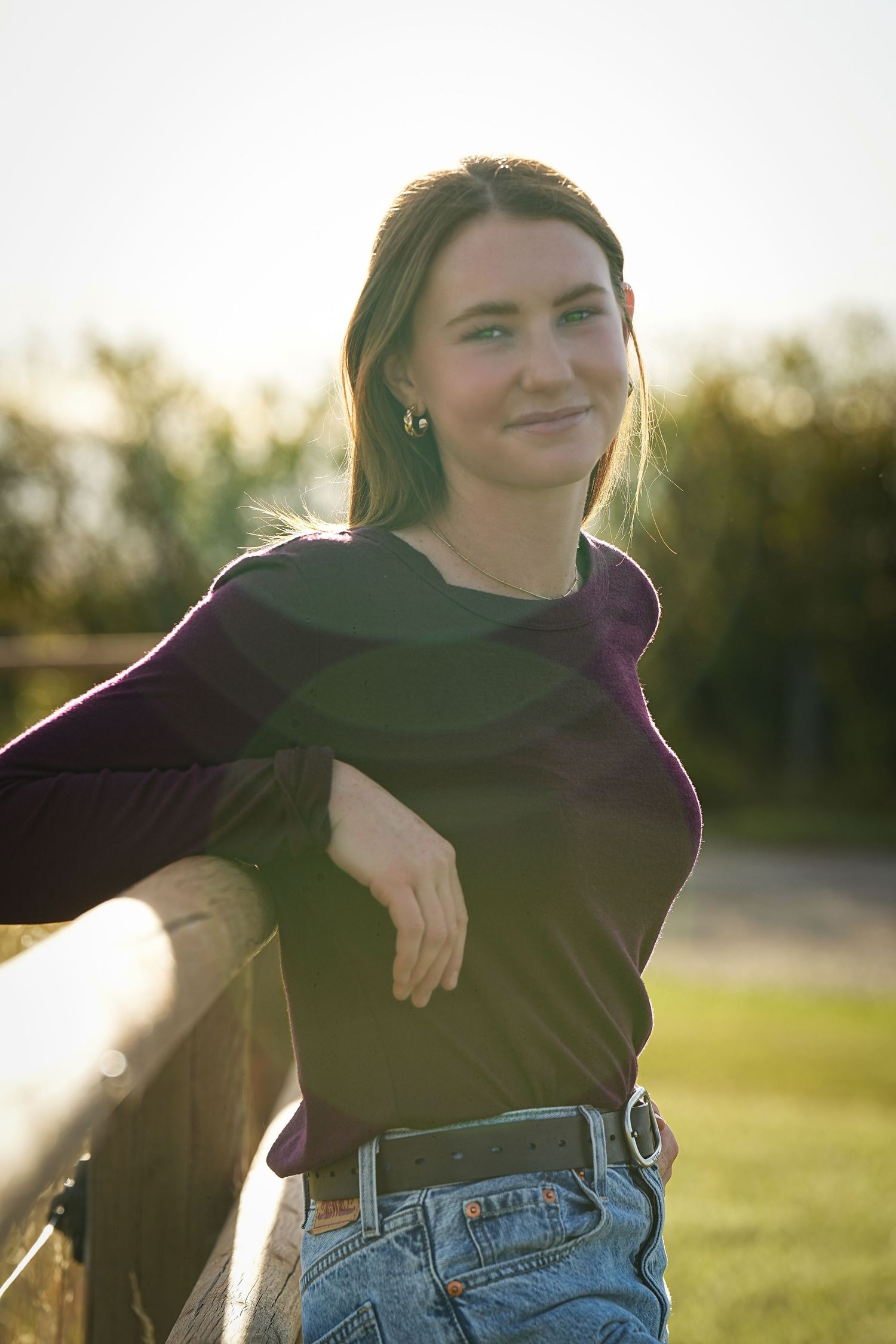 A casual portrait taken during golden hour showing someone in a dark top and jeans leaning against a fence.