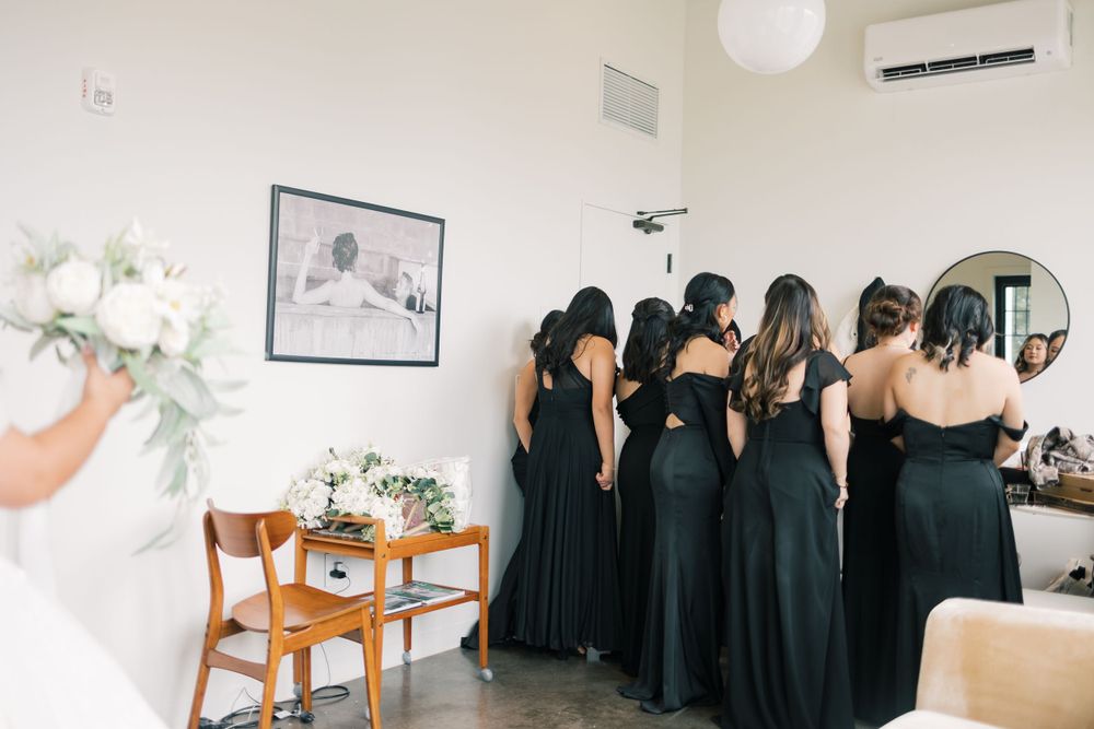 A group of bridesmaids in dark green dresses stand together in a bright room with elegant decor.