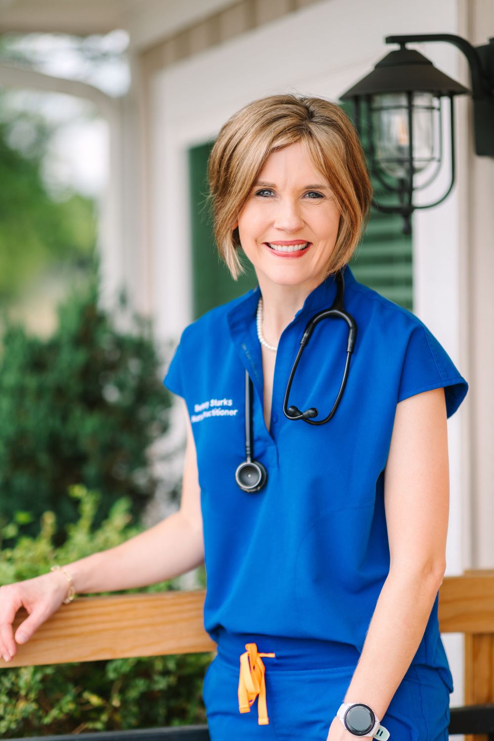 Healthcare professional in blue scrubs with stethoscope on outdoor porch.