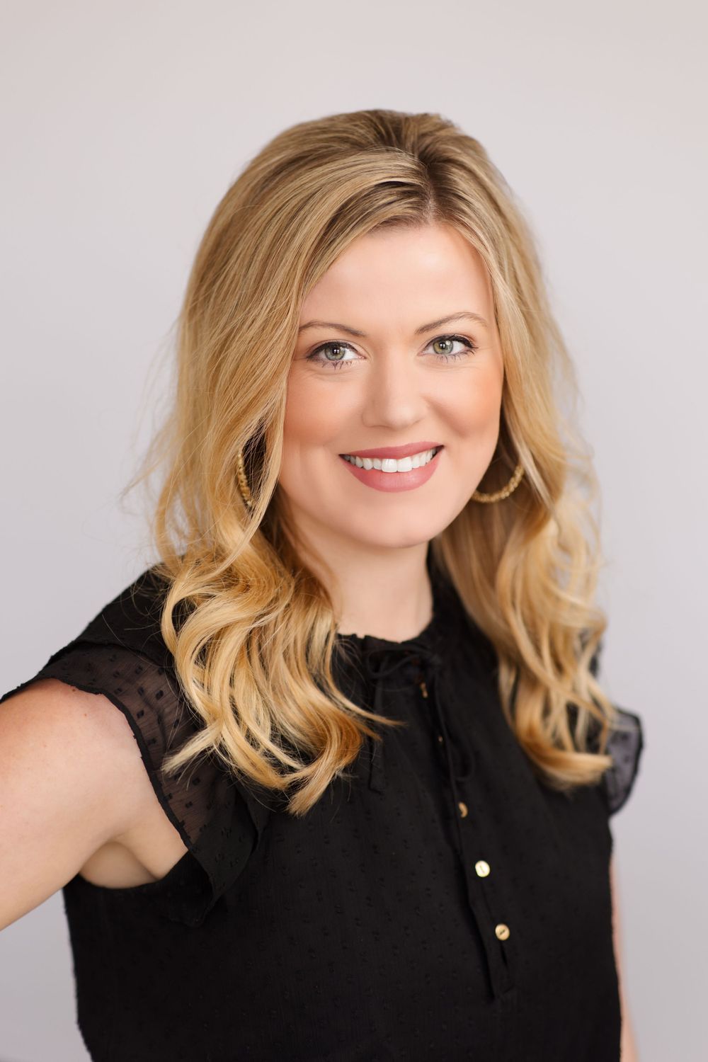 Professional studio portrait of someone in a black sleeveless top with styled blonde hair.