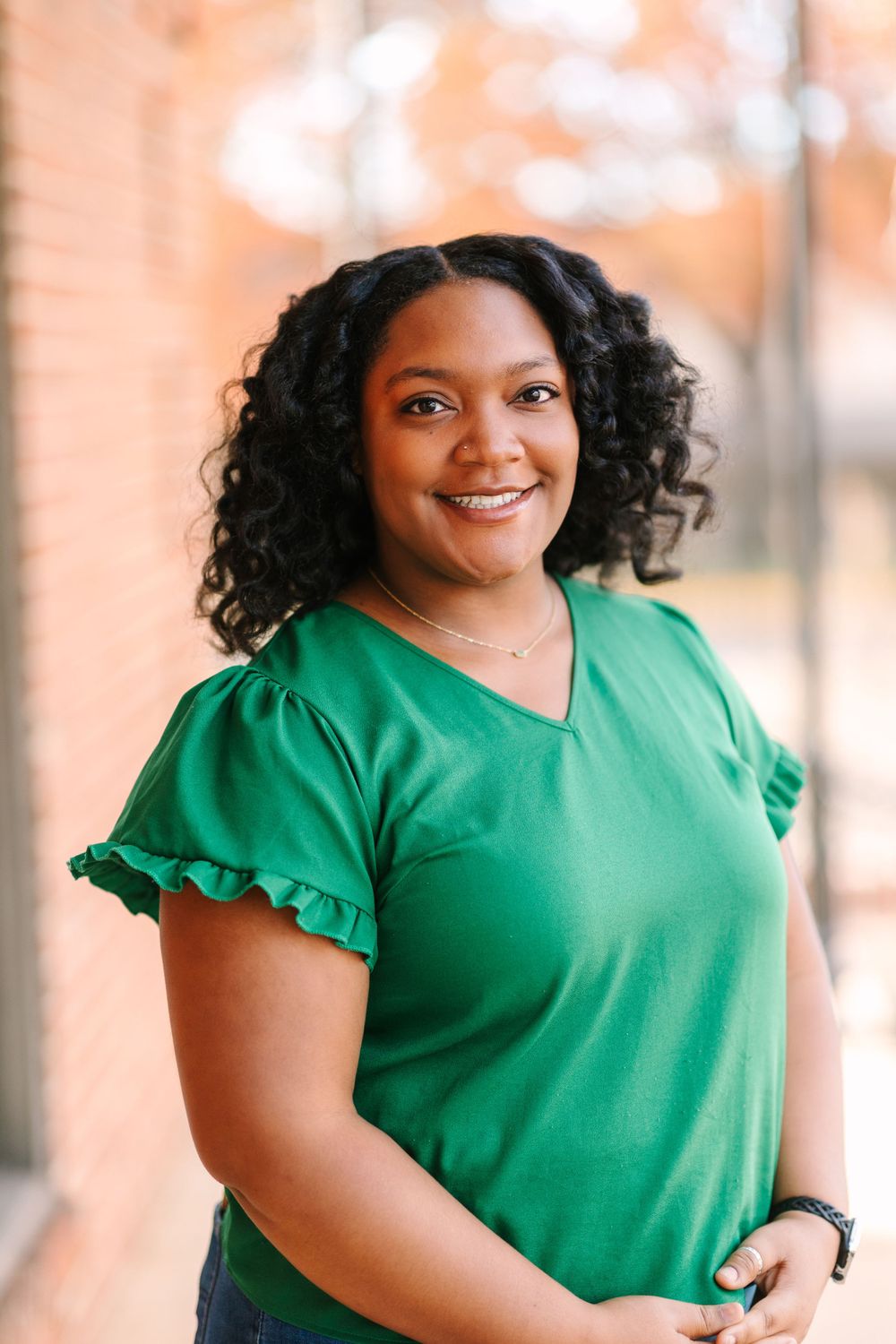 Professional portrait of someone in a green ruffled sleeve top smiling warmly at the camera.