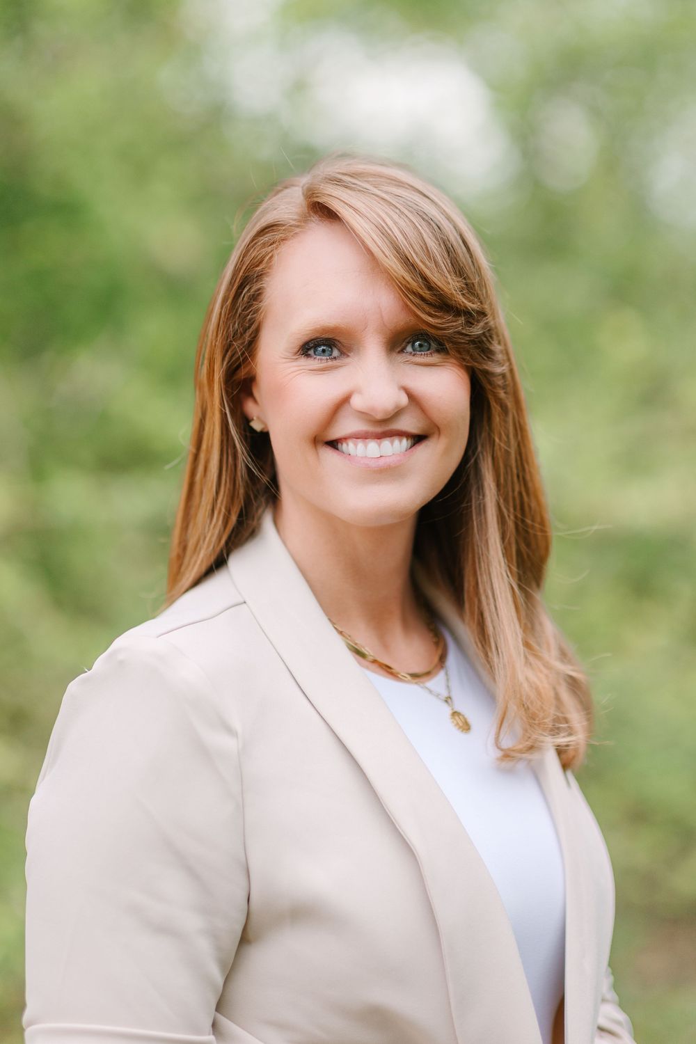 Professional outdoor portrait of a person in beige blazer and white top with natural background.