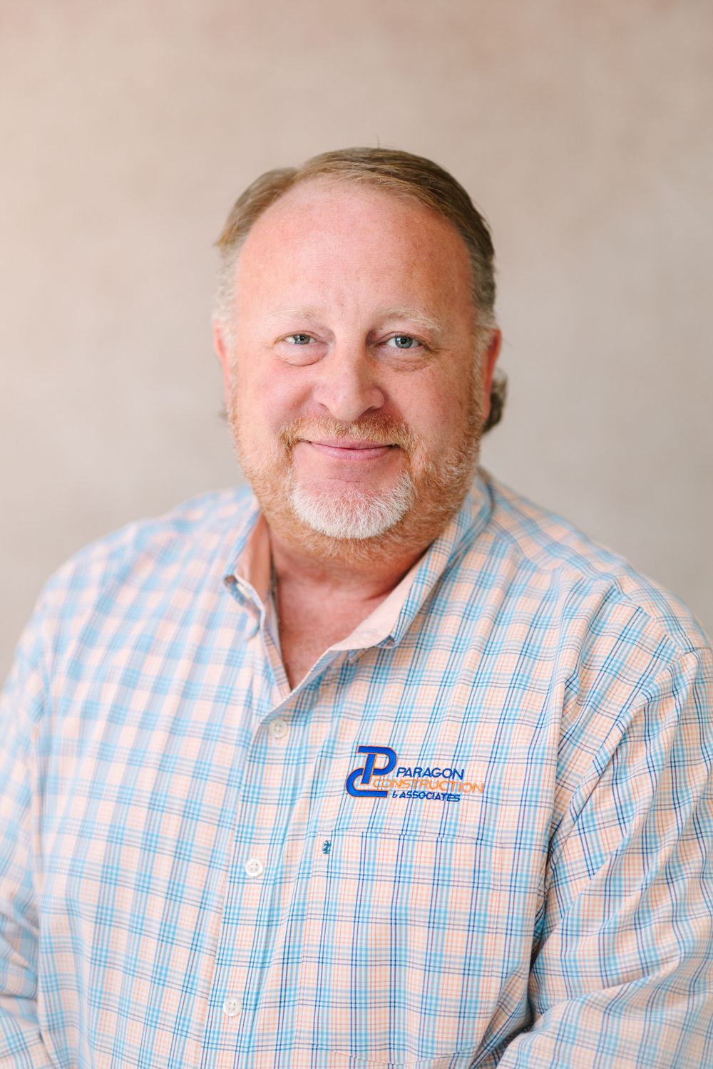 Professional headshot of someone in a checkered button-down shirt with company logo.